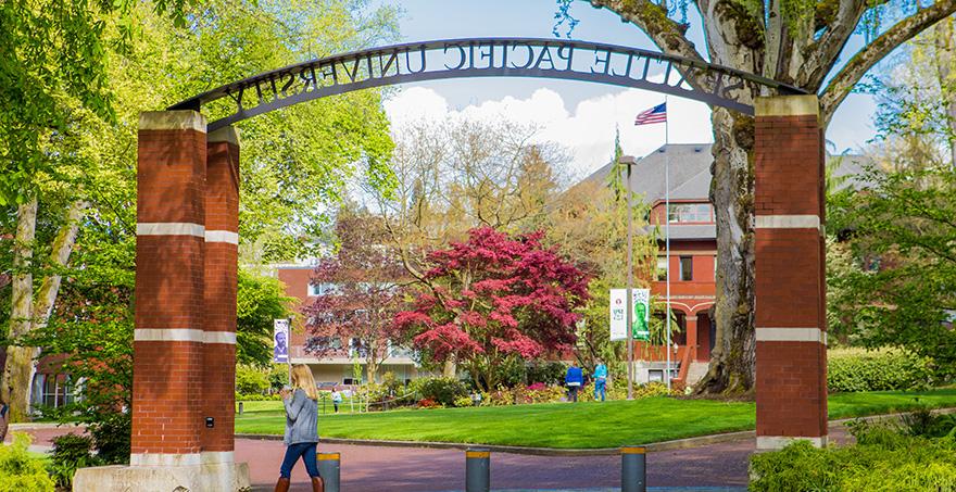 An SPU student walks by the 西雅图 Pacific University entry archway on a bright spring day